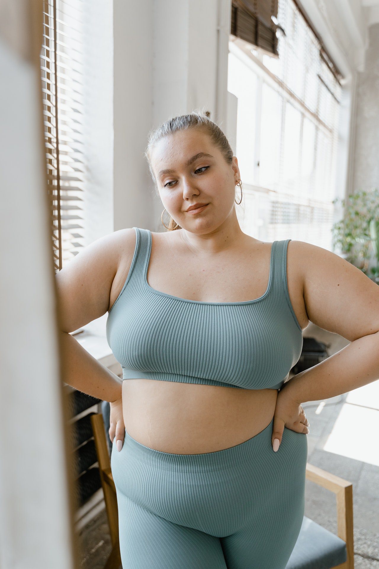 "A person measuring their waistline with a tape measure, while holding a plate of fruits and vegetables and a water bottle on a table in front of them, with a person jogging in the background